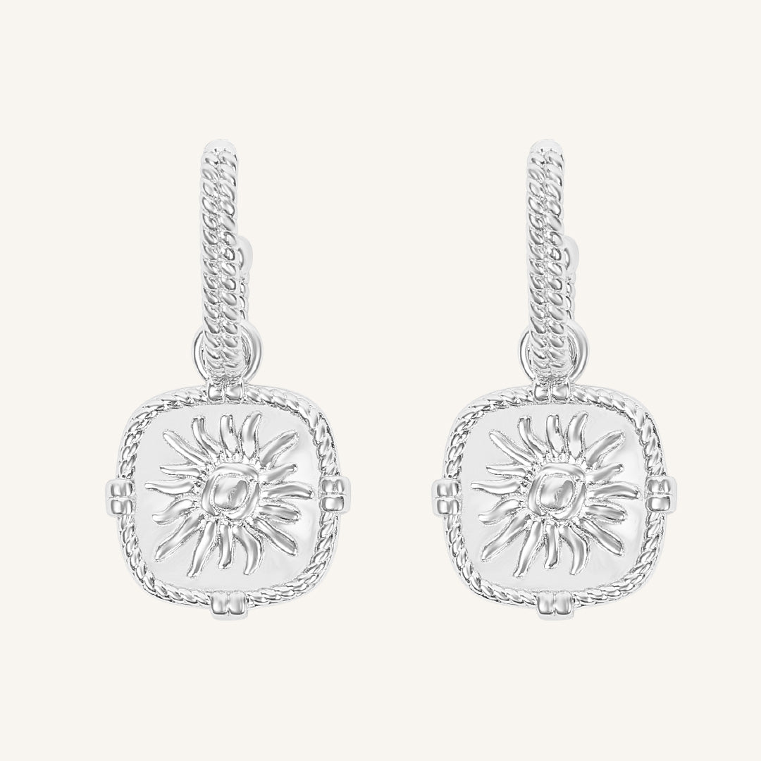 Pair of silver earrings with sun design on a white background