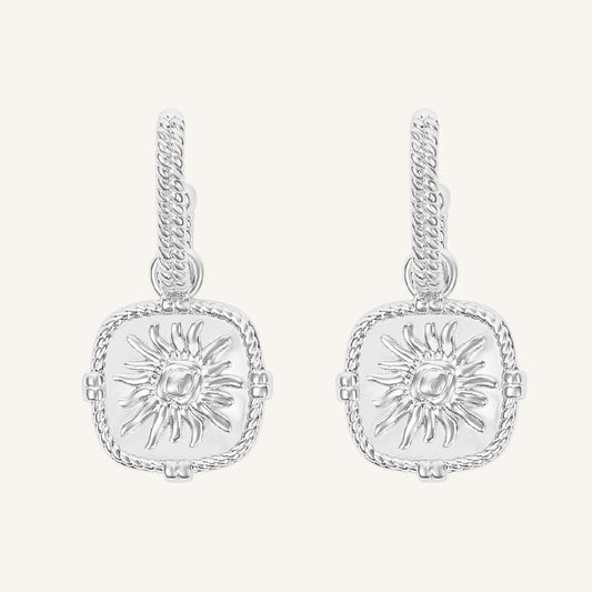 Pair of silver earrings with sun design on a white background