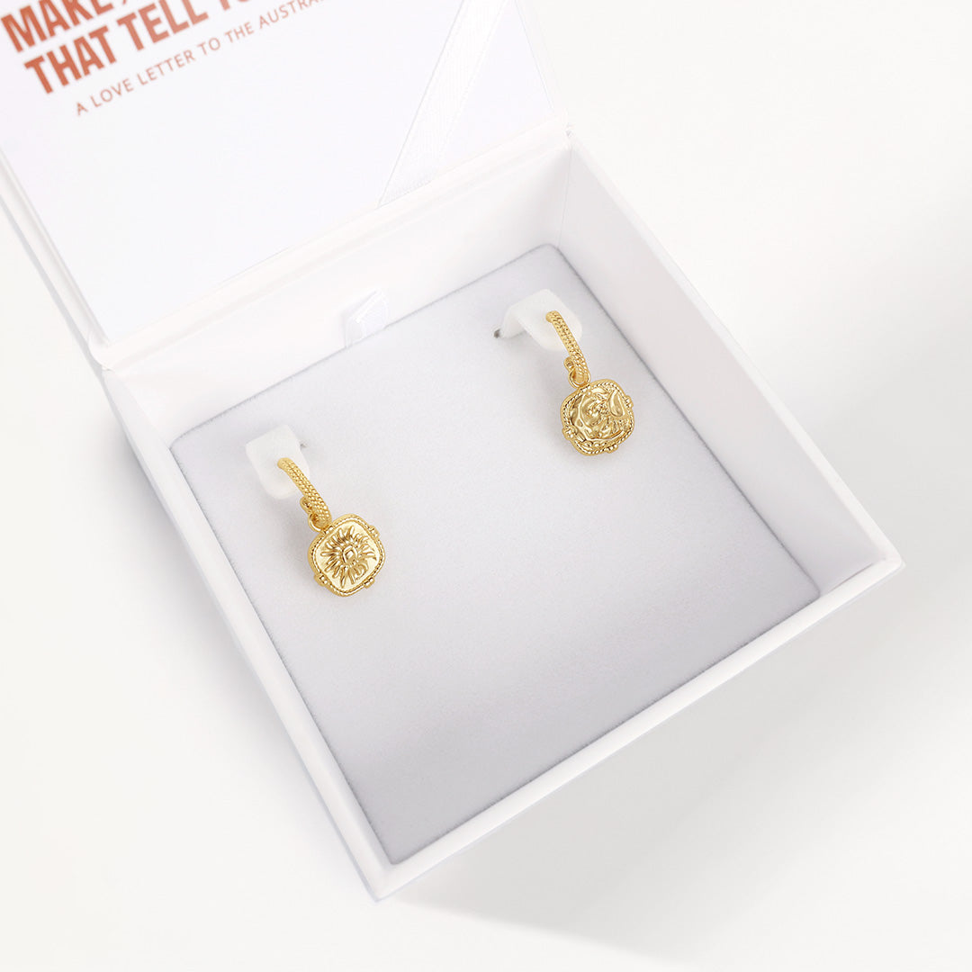Gold earrings on a white display card with text in the background