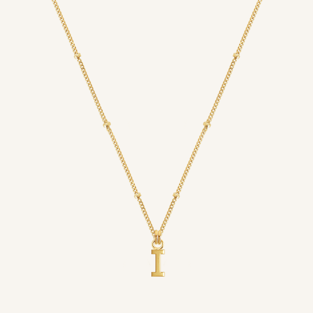 Gold necklace with a 'I' pendant on a light beige background