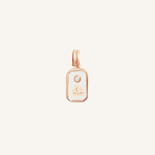 A rose gold rectangular shaped charm with the Libra zodiac symbol on it, designed with an iridescent finish.