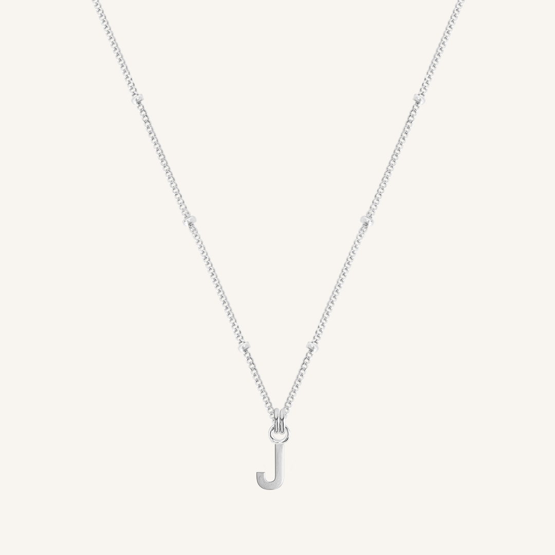 Silver necklace with a 'J' pendant on a light gray background