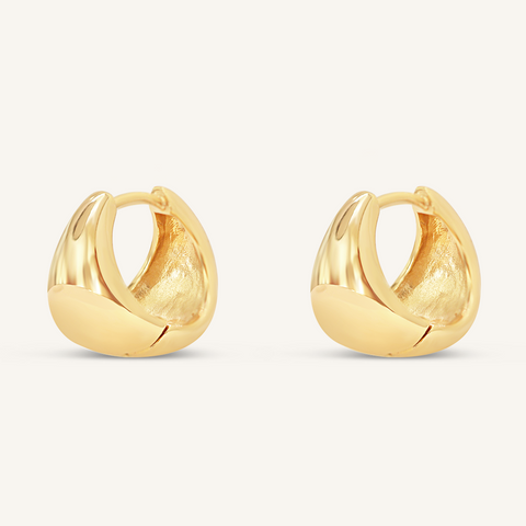 A pair of gold-colored huggie hoop earrings on a white background.