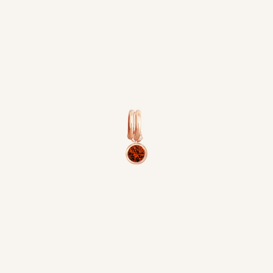 Round rose gold charm with bezel-set garnet cubic zirconia representing the January birthstone.
