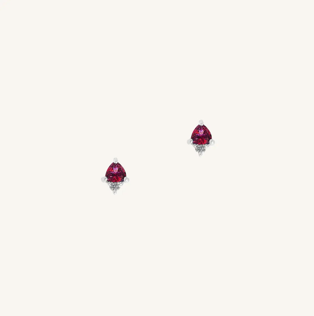 A silver pair of stud earrings featuring a red cubic zirconia, representing July.