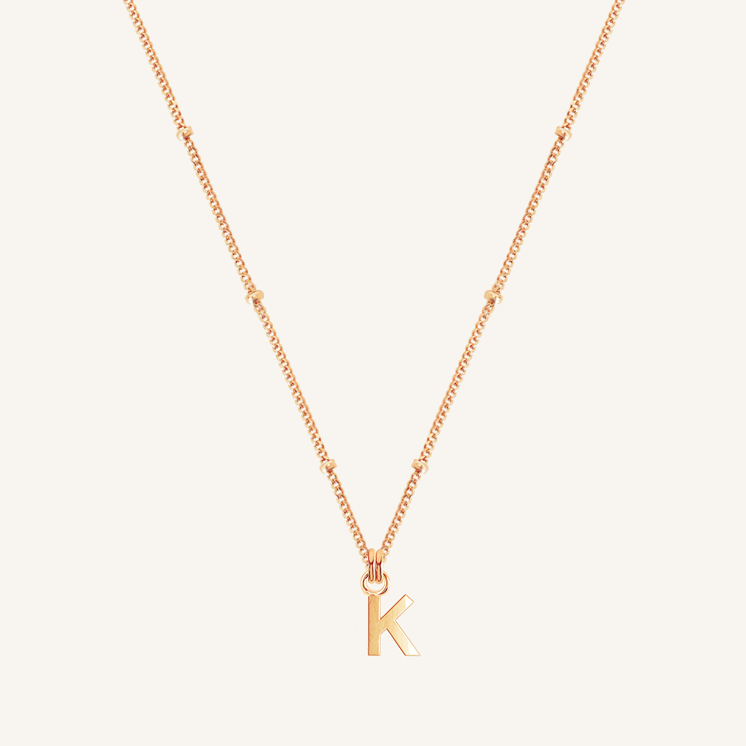 Rose gold necklace with a 'K' pendant on a light beige background