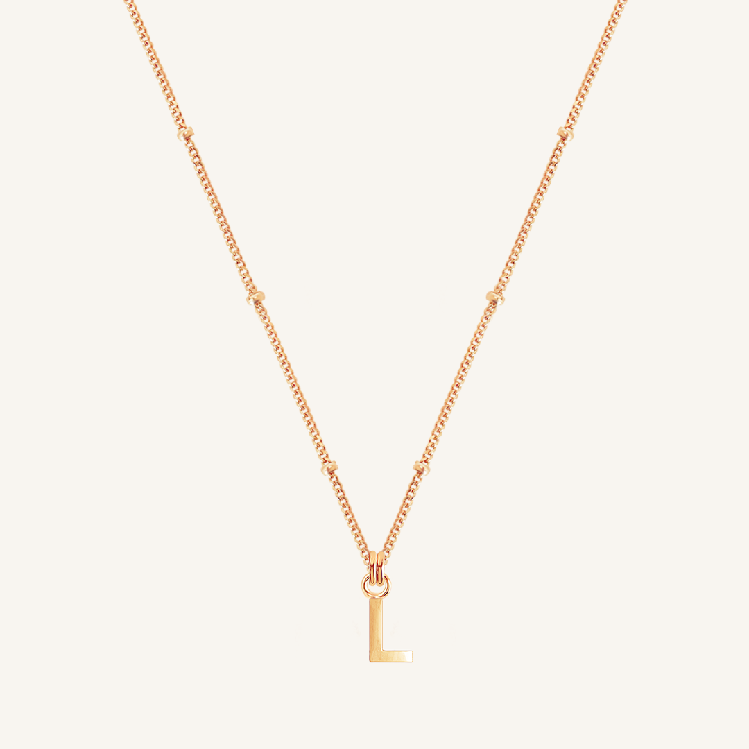 Rose gold necklace with a 'L' pendant on a light beige background