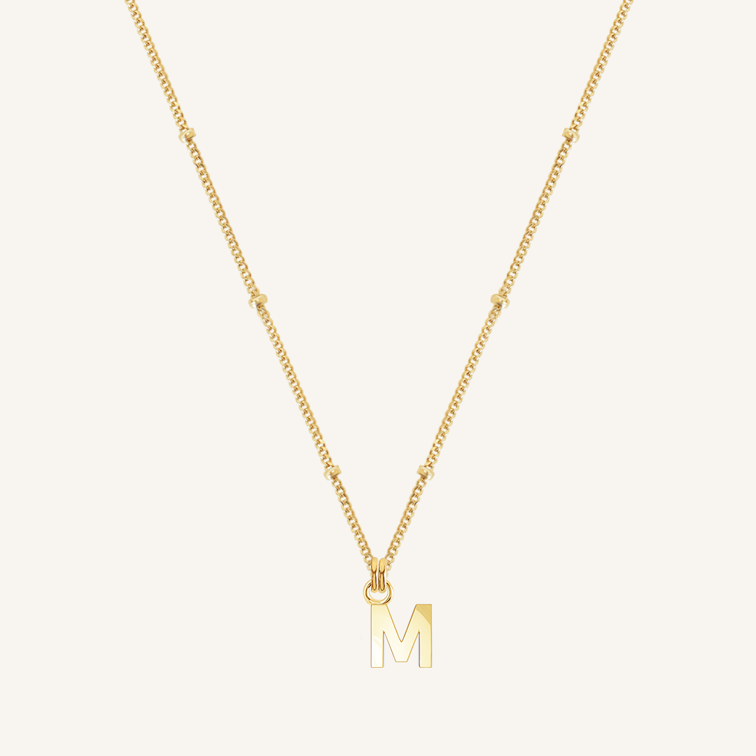 Gold necklace with a 'M' pendant on a light beige background