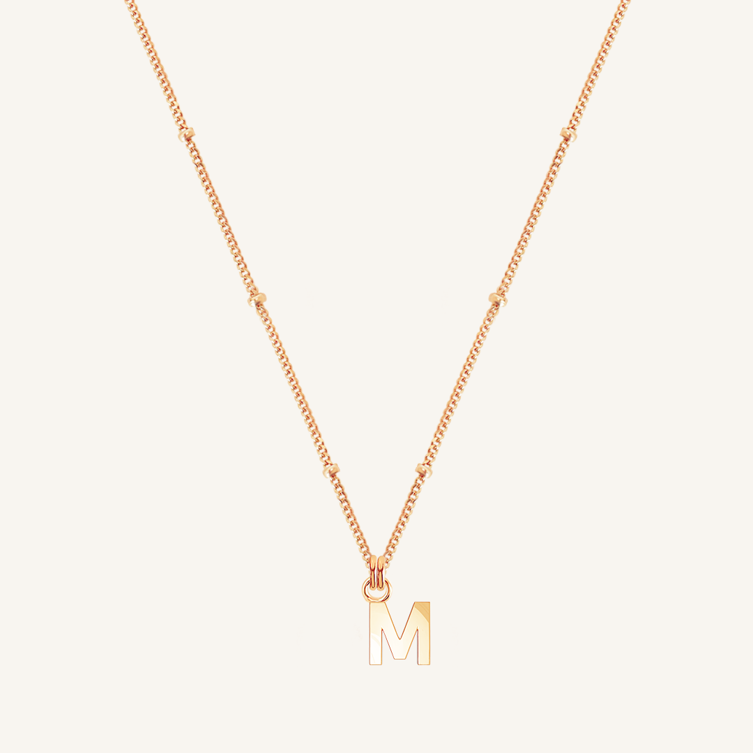 Rose gold necklace with a 'M' pendant on a light beige background