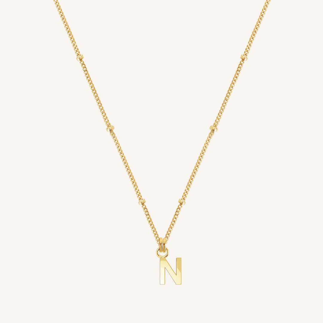Gold necklace with a 'N' pendant on a light beige background