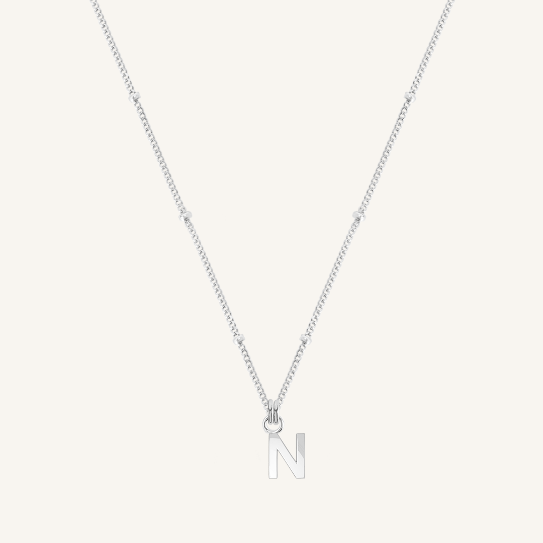 Silver necklace with a 'N' pendant on a light gray background