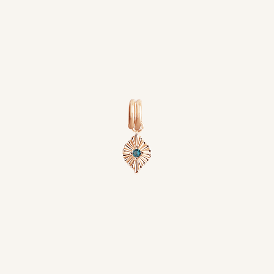 A gold-colored birthstone charm with a central blue stone surrounded by smaller clear stones, attached to a gold-colored chain.