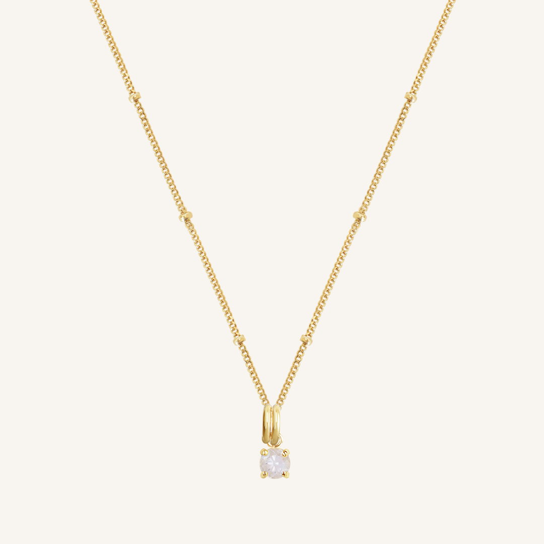 A gold-tone charm necklace with a small moonstone pendant, isolated on a white background.