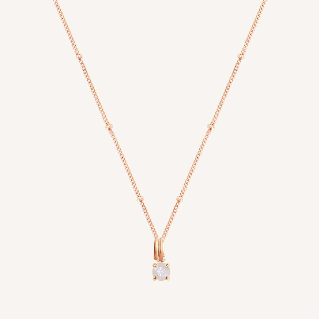 A rose charm necklace with a small moonstone pendant, isolated on a white background.