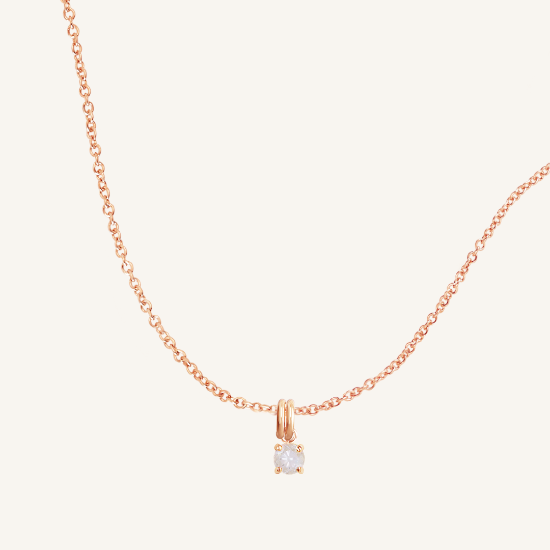 A rose charm necklace with a small moonstone pendant, isolated on a white background.