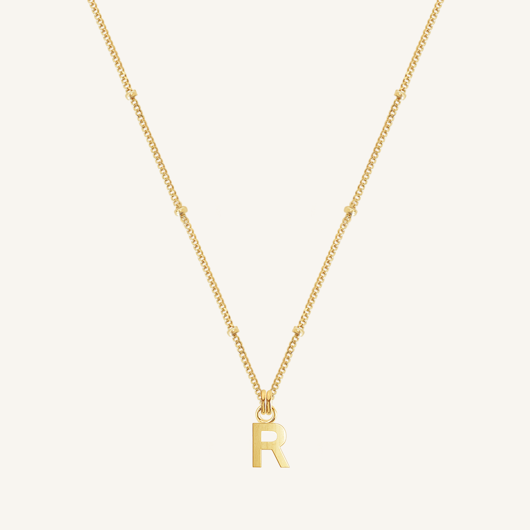 Gold necklace with 'R' pendant on a white background