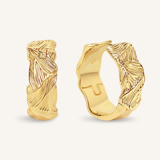 Gold hoop earrings with leaf-like designs on a white background