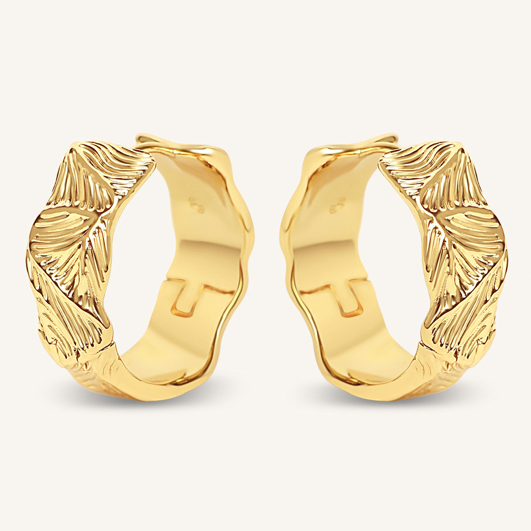 Pair of gold hoop earrings with leaf-like designs on a white background