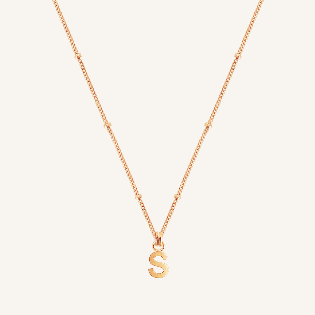 Gold necklace with a 'S' pendant on a light beige background
