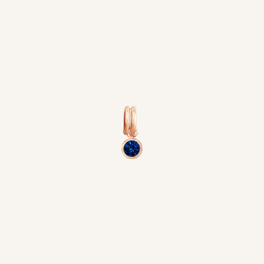 A round September birthstone charm with a blue cubic zirconia, set in rose gold.