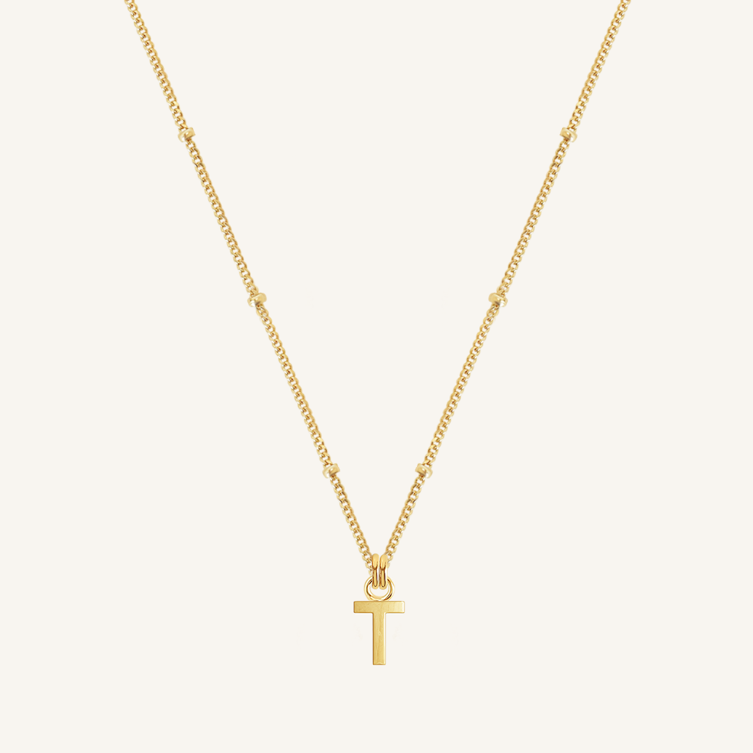 Gold necklace with a 'T' pendant on a light beige background
