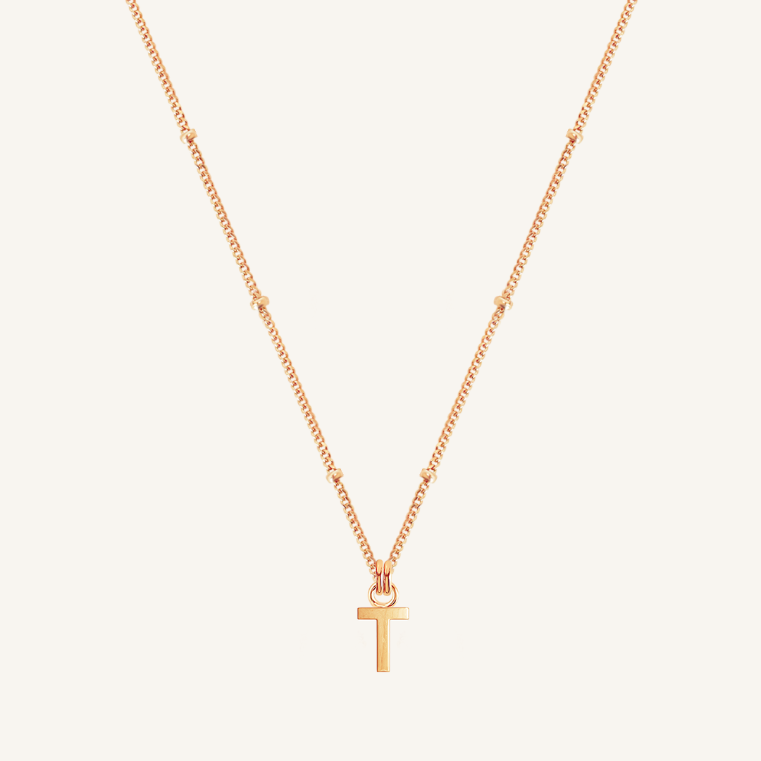 Rose gold necklace with a 'T' pendant on a light beige background
