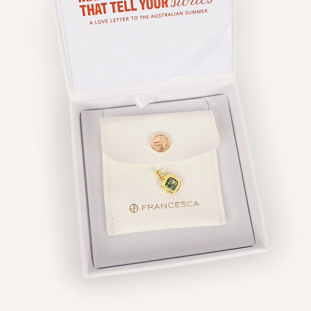 Gold earrings with a green gemstone on a Francesca branded card, displayed in a white box.