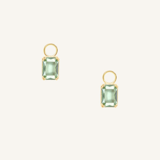 Gold hoop charms with green gemstones on a white background