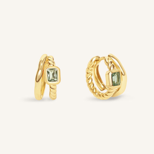 Gold hoop earrings with green gemstones on a white background