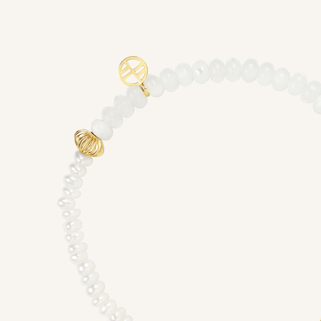 Bracelet with white beads and gold peace symbol charm on a white background