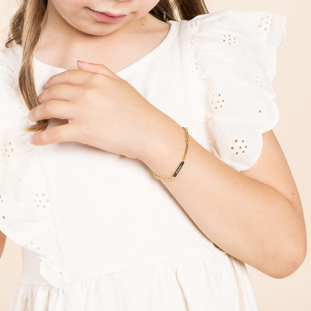 A gold-tone bracelet with a chain design and an engraving bar, worn on childs wrist 