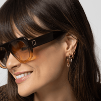 A pair of gold-colored huggie hoop earrings on a white background.