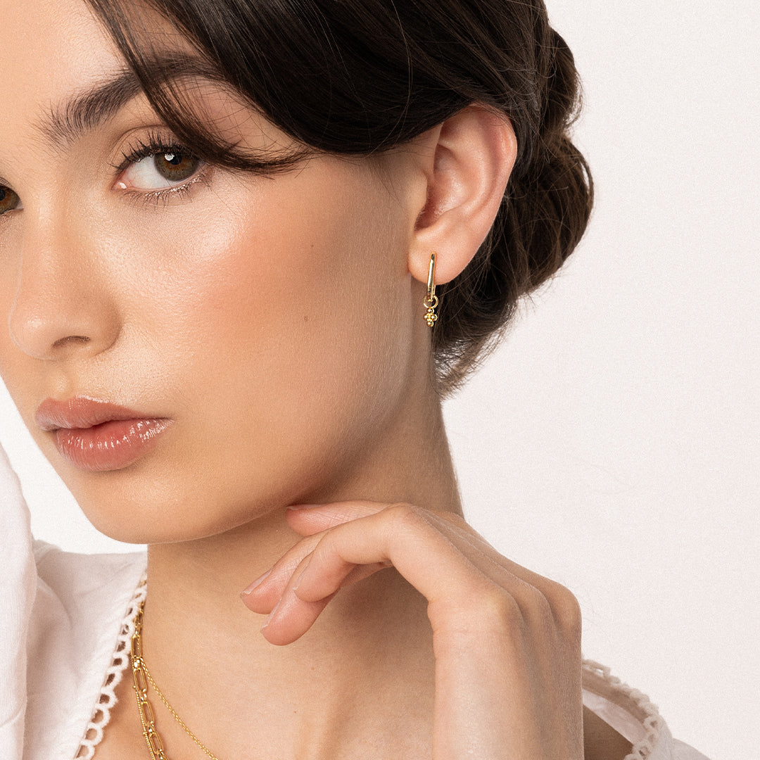 A pair of gold-tone rectangle hoop earrings with petite bobble details, worn in models ear
