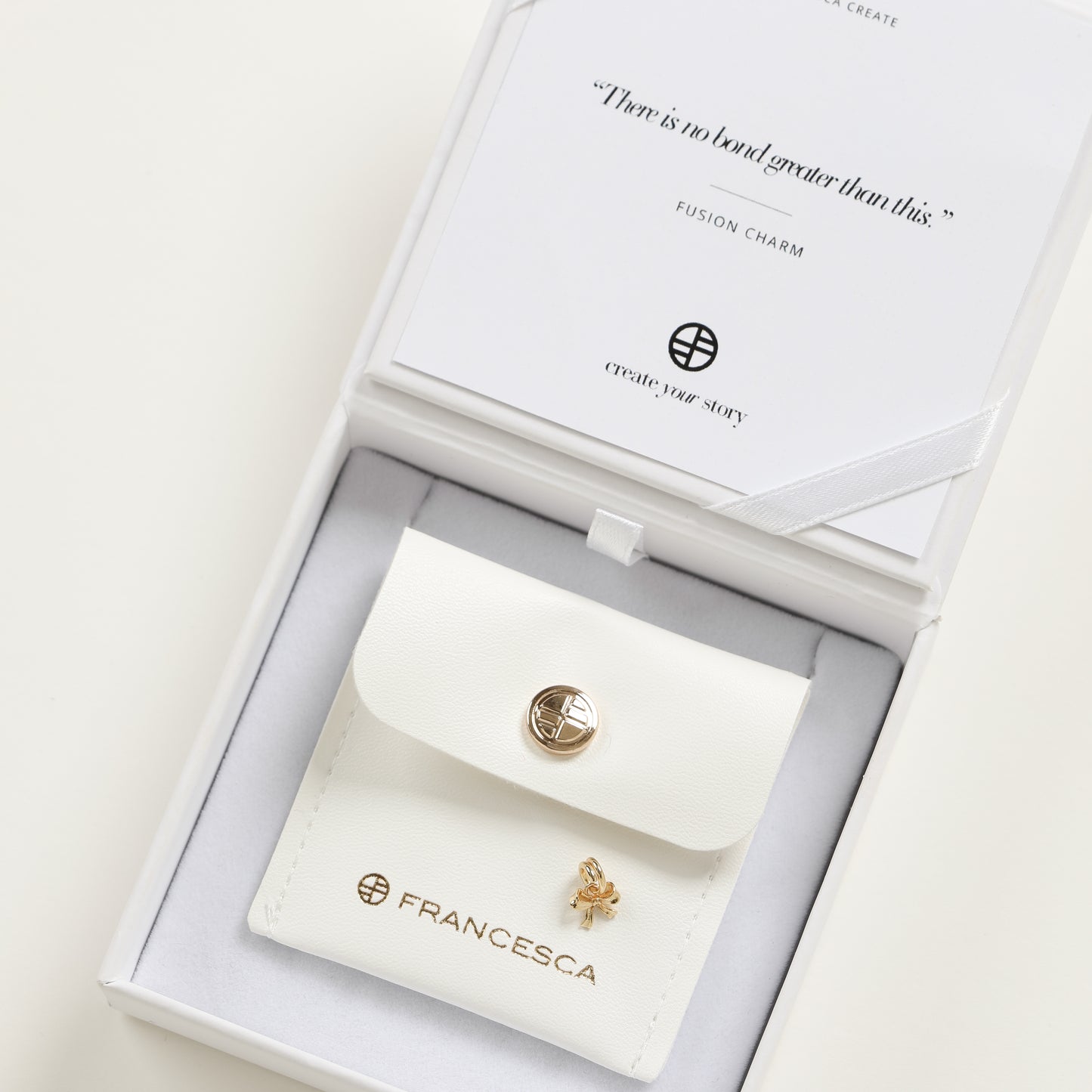 A small gold bow charm with a loop on top for attachment, displayed in a white box