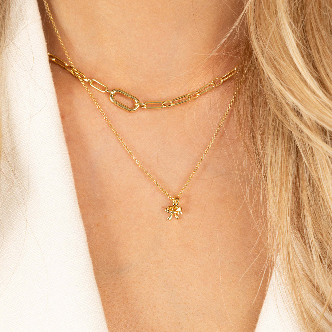 A small gold bow charm on plain chain, around models neck