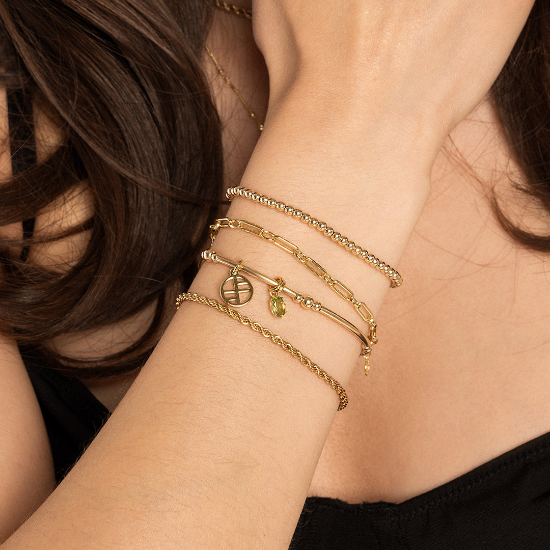 A gold-tone heritage charm bracelet with a beaded chain and a green oval charm, on wrist