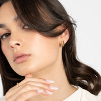 A pair of gold-coloured hoop earrings with a huggie design, featuring a layered look and pave white stones on one side.