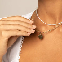 A silver heart-shaped necklace with a chain, featuring an engraved monogram initials and a date on the front.