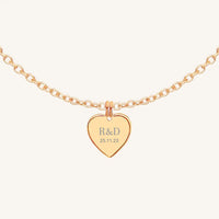A rose heart-shaped necklace with a chain, featuring an engraved monogram initials and a date on the front.