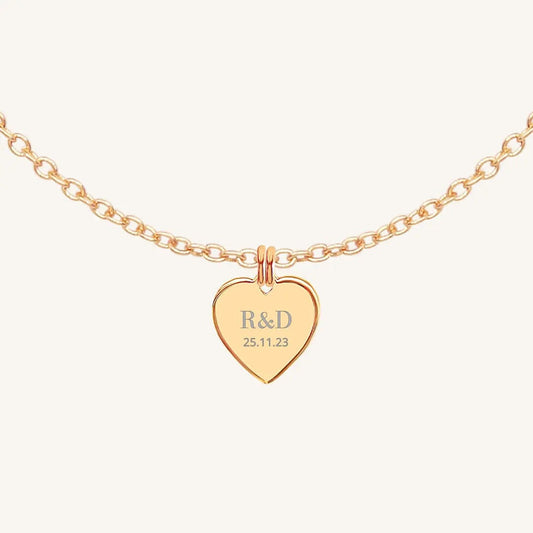 A rose heart-shaped necklace with a chain, featuring an engraved monogram initials and a date on the front.