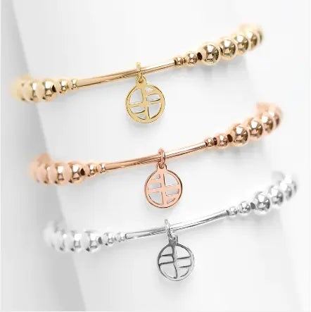 A gold-tone charm bracelet with a beaded design and a circular charm hanging from a bar, displayed with other bracelets